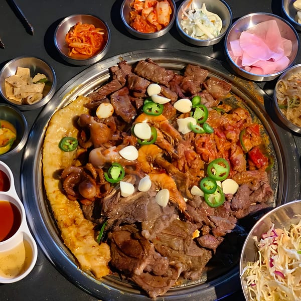A Korean BBQ grill filled with various meats, seafood, garlic, and jalapeños, surrounded by banchan.
