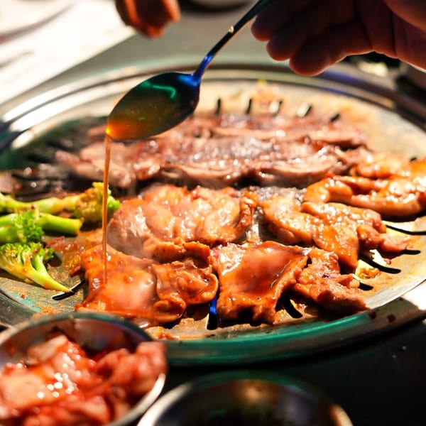 Marinated Korean BBQ meat and broccoli cooking on a grill, with sauce being spooned over.