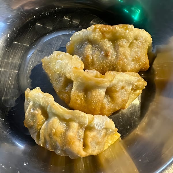 Three golden-brown fried Korean dumplings, or mandu, rest in a shiny metal bowl.