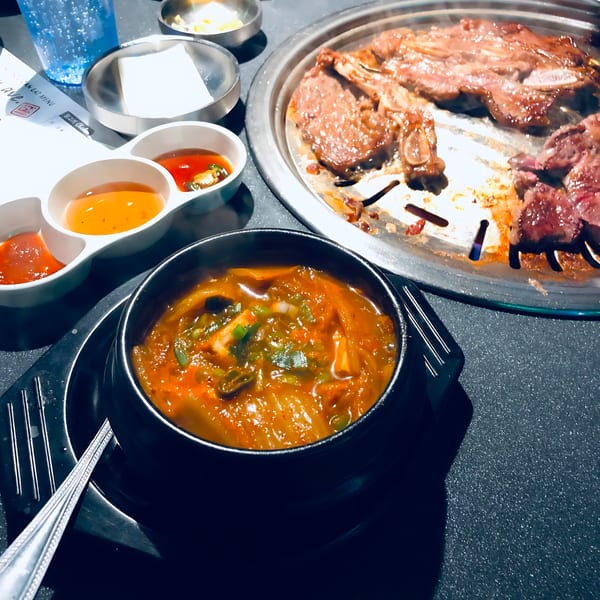 Kimchi stew and grilling Korean BBQ short ribs with dipping sauces on a dark table.