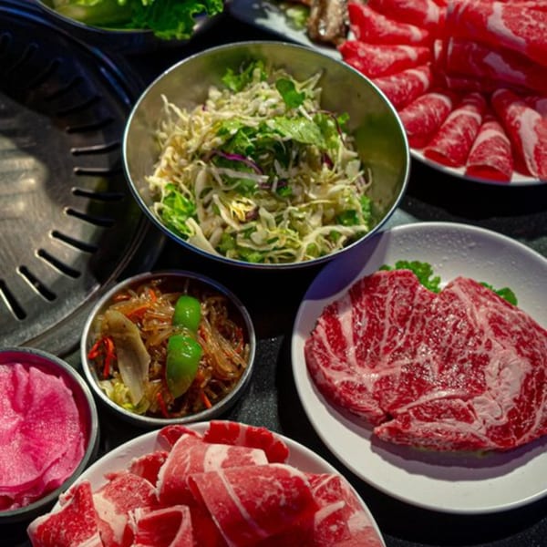 Assortment of raw beef cuts and Korean side dishes, including salad and pickled vegetables, ready for grilling.